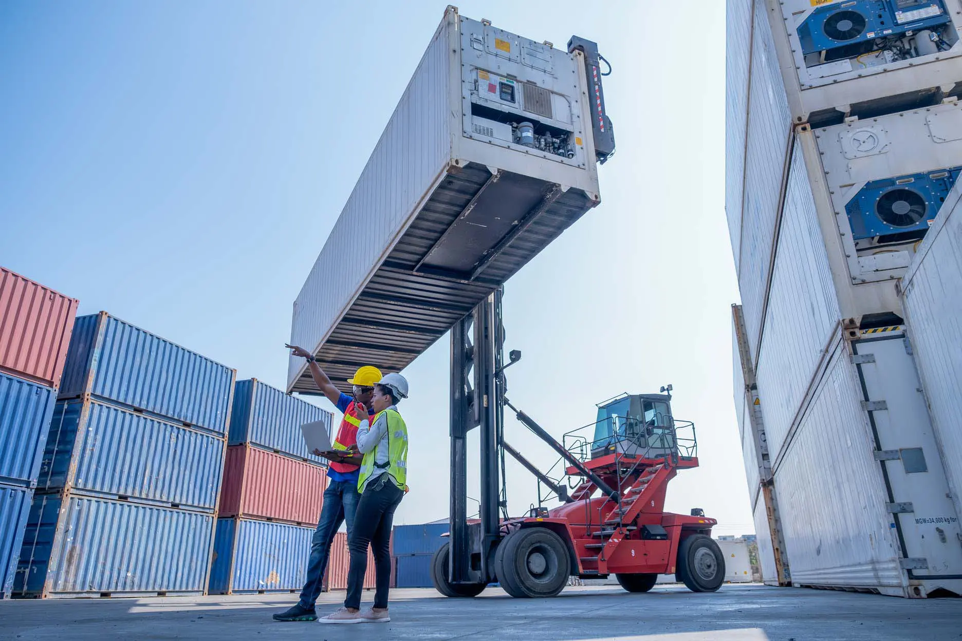 Twee personen die voor een heftruck met een koelcontainer staan op een containerterrein